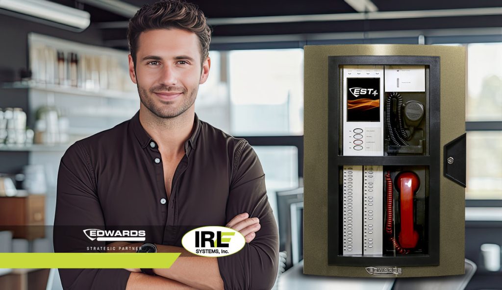 Man smiling next to EST4 Fire Alarm System, featuring modern design and integrated controls, with IRL Systems branding and Edwards partnership logo, in a contemporary office setting.