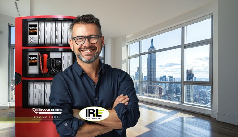 Smiling man in a modern interior with fire alarm equipment, showcasing Edwards EST4 systems and IRL Systems branding, emphasizing fire safety solutions for Brooklyn's multi-residential buildings.